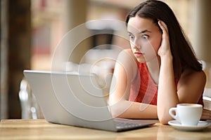 Shocked woman watching laptop content in a bar