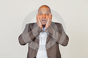 Shocked young african american guy businessman expressing surprise and amazement, touching his face and folding his lips, stands