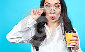 Shocked young asian girl with glasses holding yellow cup of coffee
