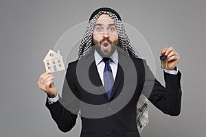 Shocked young bearded arabian muslim businessman in keffiyeh kafiya ring igal agal classic black suit isolated on gray