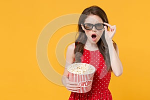 Shocked young brunette woman girl in red summer dress, 3d glasses posing isolated on yellow wall background. People