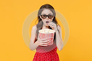 Shocked young brunette woman girl in red summer dress, 3d glasses posing isolated on yellow wall background. People