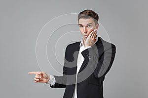 Shocked young business man in classic black suit shirt isolated on grey wall background. Achievement career wealth