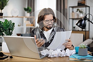 Shocked young caucasian man sitting at table with modern laptop at home office