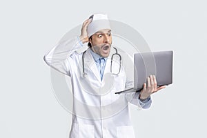 Shocked young doctor looking at laptop in amazement