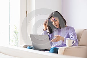 Shocked young ethnicity woman looking in computer and fixing her glasses. Lockdown news, online shocking low price