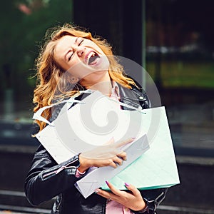 Shocked young fashion girl wearing black leather jacket and holding shopping bags. Seasonal sales, discounts. Happy woman after