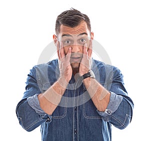 Shocked: young man in blue denim shirt with hands touching face