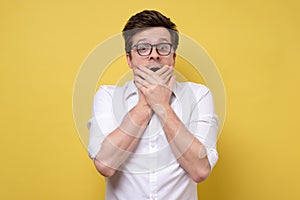 Shocked young man covering mouth with hands and looking at camera stunned