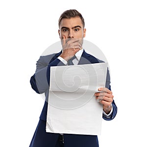 Shocked young man in elegant suit reading newspaper