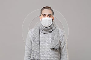 Shocked young man in gray sweater, scarf isolated on grey background studio portrait. Healthy lifestyle, ill sick