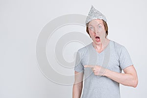 Shocked young man with tinfoil hat as conspiracy theory concept pointing to side