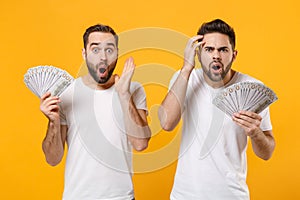 Shocked young men guys friends in white blank empty t-shirts isolated on yellow orange wall background. People lifestyle