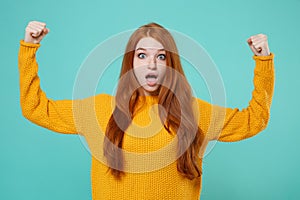 Shocked young redhead woman girl in yellow sweater posing isolated on blue turquoise background studio portrait. People