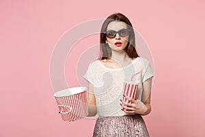 Shocked young woman in 3d imax glasses posing isolated on pastel pink background. People sincere emotions in cinema