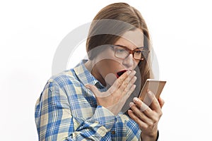 Shocked young woman in blue plaid shirt holding smartphone in hands
