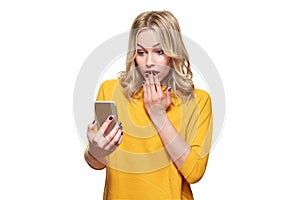 Shocked young woman holding up her mobile phone, reading shocking news. Woman in disbelief, isolated over white background.