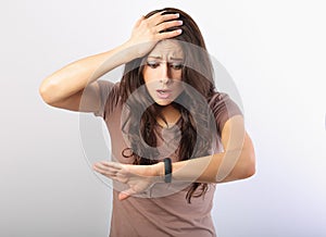 Shocked young woman looking on the hand with wrist watch with unhappy worried eyes on blue background. Closeup