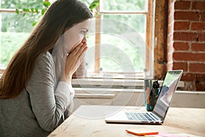 Shocked young woman looking at laptop screen at work desk.