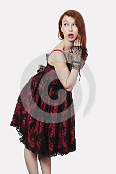 Shocked young woman in retro styled lace dress against gray background