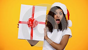 Shocked young woman in santa claus hat showing huge gift box, christmas present