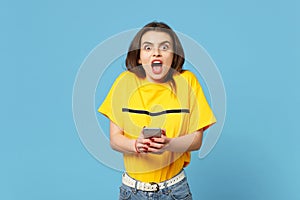 Shocked young woman in vivid casual clothes keeping mouth open, using mobile phone, typing sms message isolated on