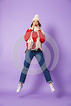 Shocked young woman wearing winter hat isolated over purple background