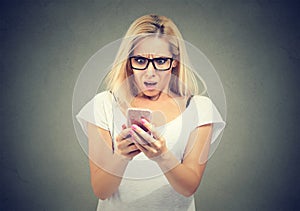 Shocking message. Surprised blond hair woman holding mobile phone and staring at it