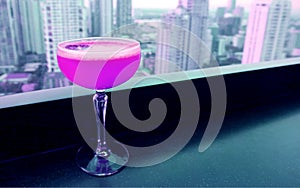 Shocking pink colored cocktail on the rooftop bar`s table with skyscrapers view in the backdrop