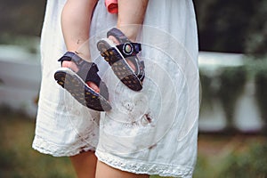 Shod feet of a child in the arms of a mother, a white dress, stained with shoes, raising children and loving them