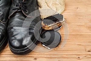 Shoe polish with brush, cloth and worn boots on wooden platform