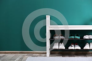 Shoe rack with different footwear near color wall. Stylish hallway interior