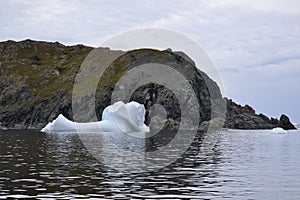 Shoe-shaped iceberg next to rugged cliffs in Twillingate Harbour