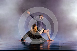 Shoeless dance couple performing multiple unique dance moves in front of a black background surrounded by a lot of smoke