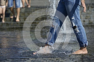 Shoeless girl feet playing with fountain water jets at the square