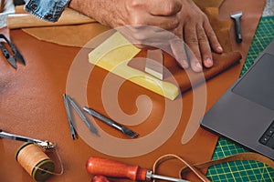 Shoemaker crafting leather using traditional tools and laptop in workshop