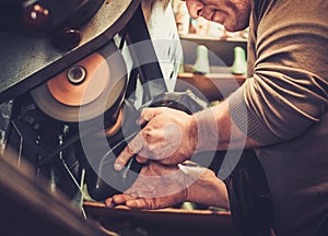 Shoemaker repairs shoes in studio craft grinder machine.