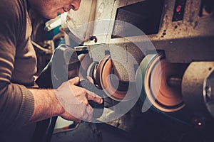 Shoemaker repairs shoes in studio craft grinder machine.