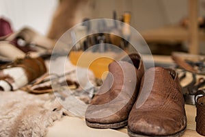 Shoemaker working desk with focus on ready shoes foreground and set of tools, material background, selective focus