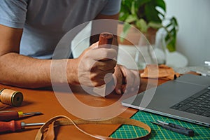 Shoemaker working leather with craft tools and laptop in his workshop