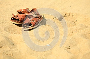 Shoes. Brown leather sandals on a sandy beach. Summertime.