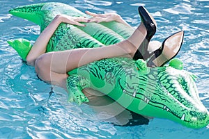 Shoes from crocodile leather. Woman legs hold mattress in swimming pool. Fashion shoes from crocodile skin. Fashion girl