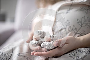 Shoes for the future baby in the hands of young pregnant woman