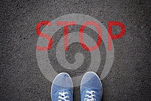 Shoes standing before stop sign painted on asphalt, top view