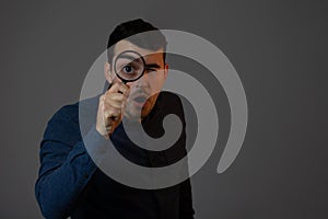 Shoked man with magnifying glass on grey background. Curious young man with magnifying glass Isolated on grey background photo