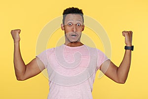 Shoked successful african american young man screaming with hands up over yellow background.