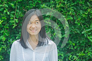 Shoot photo Asian woman portrait wear white shirt, smiling and looking sideways with green tree background.