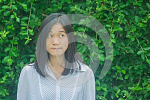 Shoot photo Asian woman portrait wear white shirt, thinking and looking sideways with green tree background.