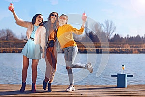 Shoot of three beautiful girls outdoors by the river. Female friends relaxing by the river and smiling. Girlfriends are stand