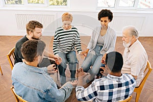 Shooting from above of diverse men and women sitting in circle during group therapy, supporting each other, holding